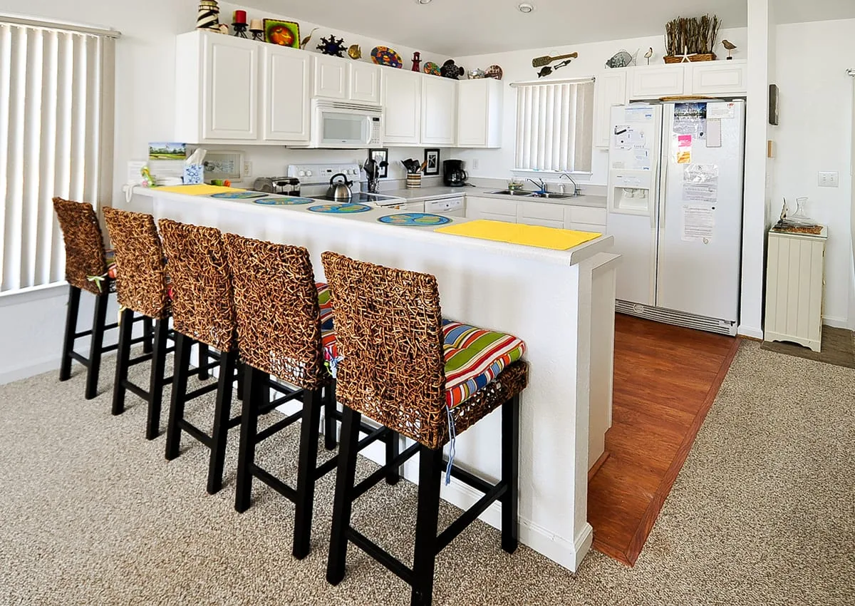 A bright kitchen with a white counter and patterned bar seating.