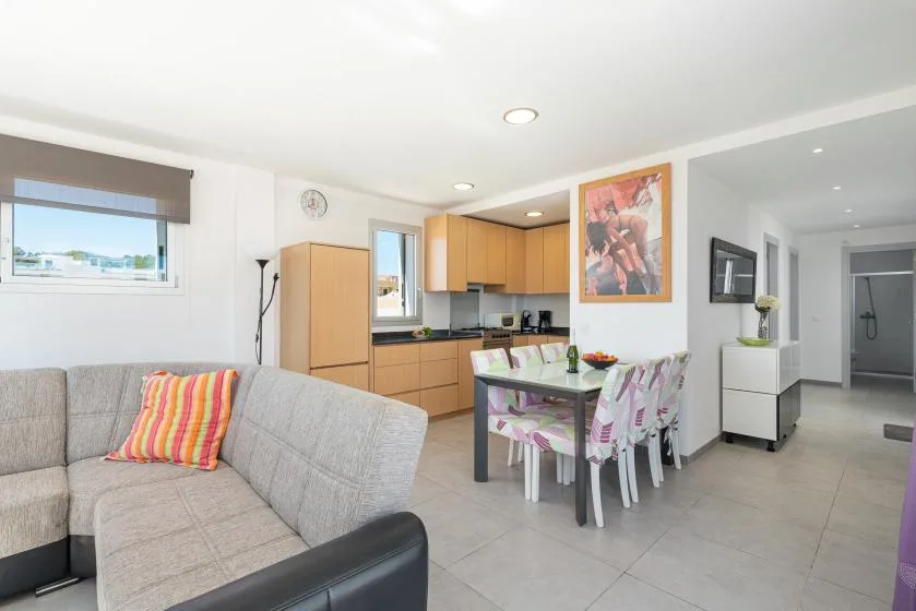 An open-plan living and dining area with a kitchen and colorful dining chairs.