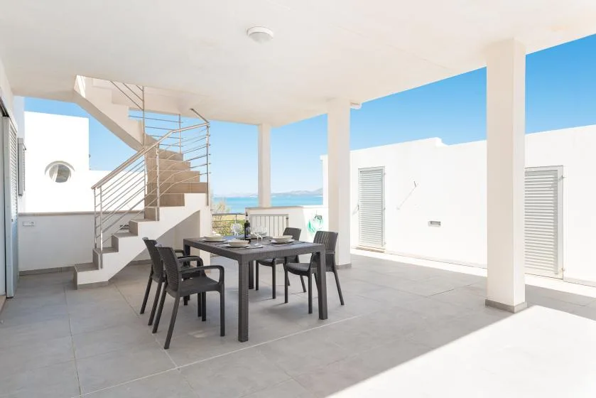 A covered outdoor dining area with a table, seating, and a view of the sea.