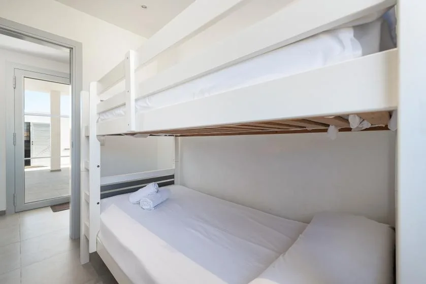 A bedroom with white bunk beds and neatly arranged bedding.