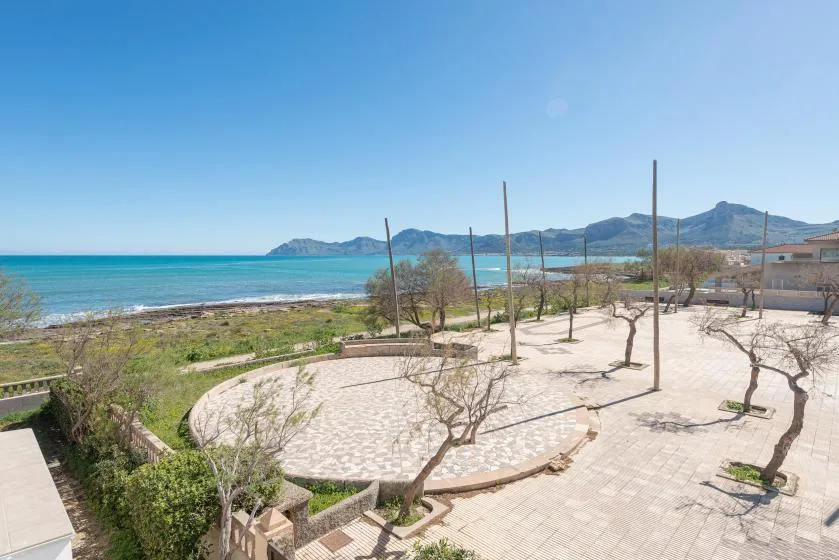 A paved coastal terrace with sparse trees overlooks the sea and distant hills.