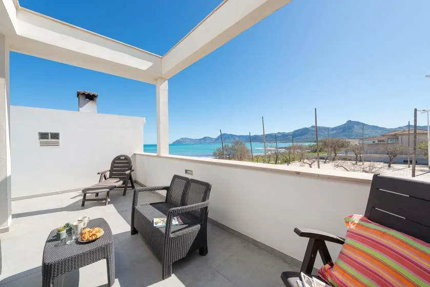 A sunny outdoor terrace with seating overlooks the sea and distant hills.