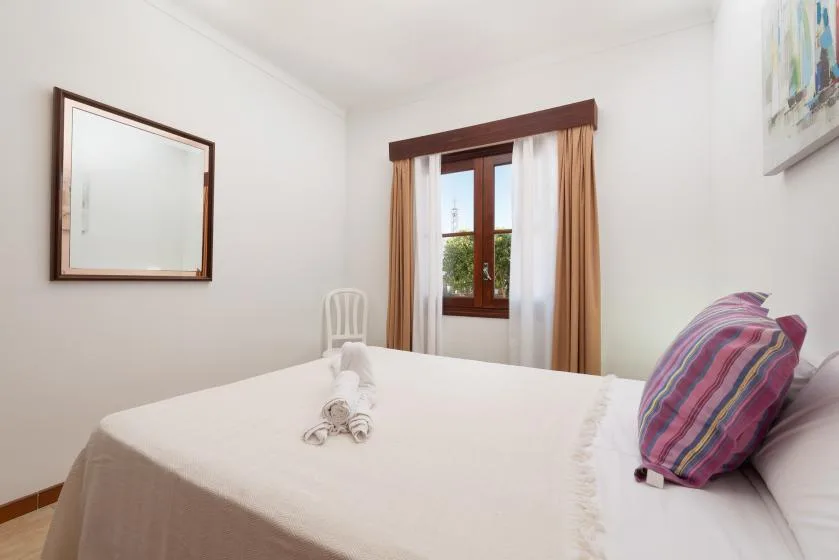 A bright bedroom with a neatly made bed and a window framed by curtains.