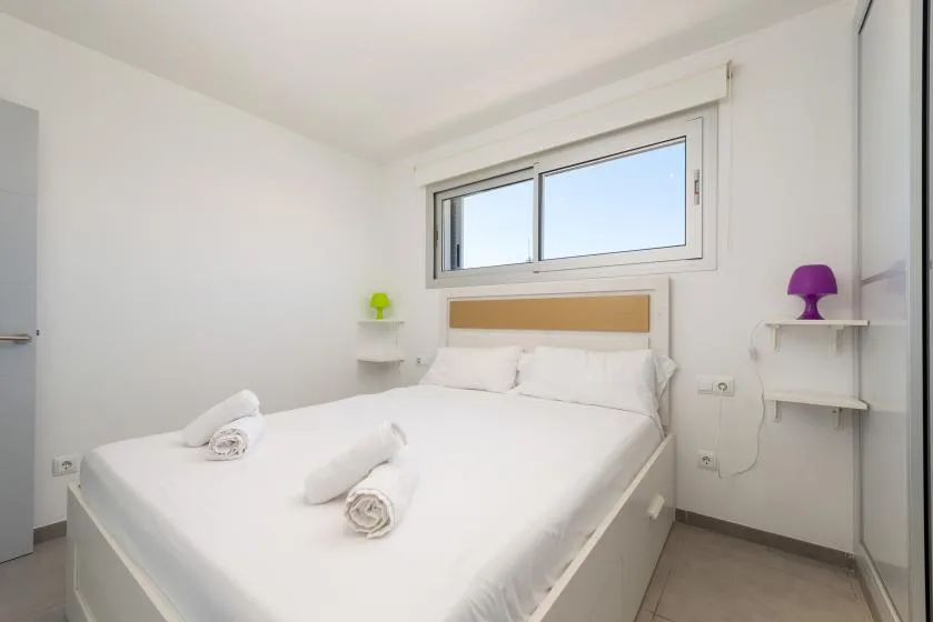 A bright bedroom with a white bed beneath a wide window.