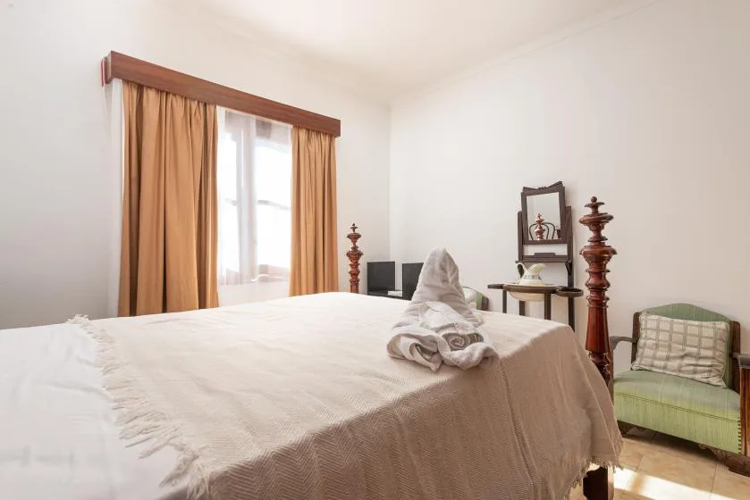 A bright bedroom with a neatly made bed and a window with curtains.