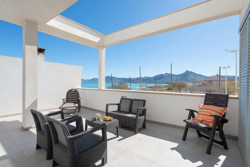 An outdoor terrace with seating overlooks the sea and distant hills.