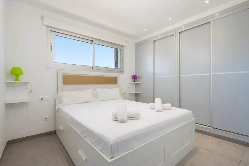 A bright bedroom with a white bed and sliding closet doors.