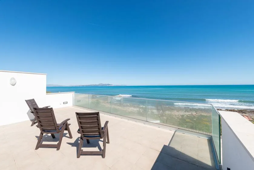 Una terraza abierta con asientos de descanso y una barandilla de vidrio da al mar.