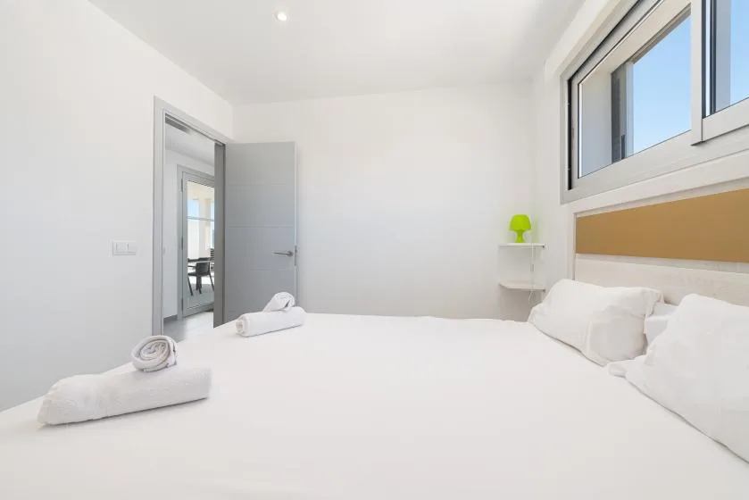 A bright bedroom with white bedding and a high window.