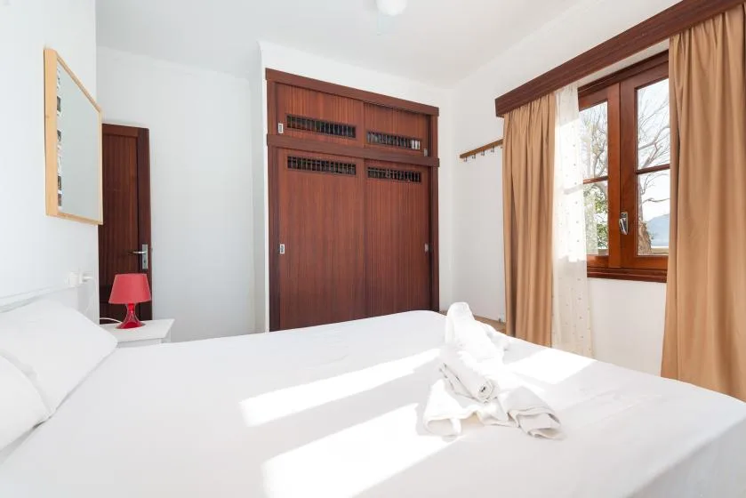 A bright bedroom with a white bed and a wood-framed window.