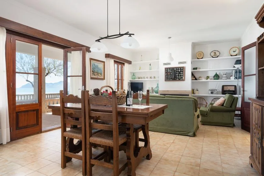 A dining and living area with a wooden table, green seating, and open shelves.