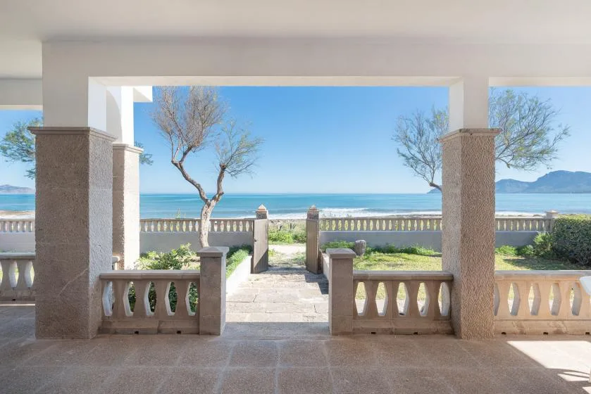 A covered patio opens onto a stone walkway and a view of the sea.