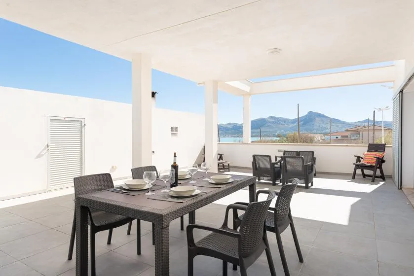 A covered outdoor dining area with a table and seating overlooking the mountains.