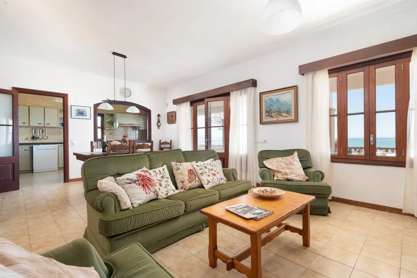 A living room with green seating, a wooden coffee table, and windows overlooking the sea.