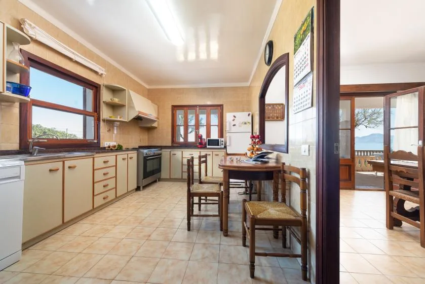 A tiled kitchen with counters and cabinets, opening onto a dining area.