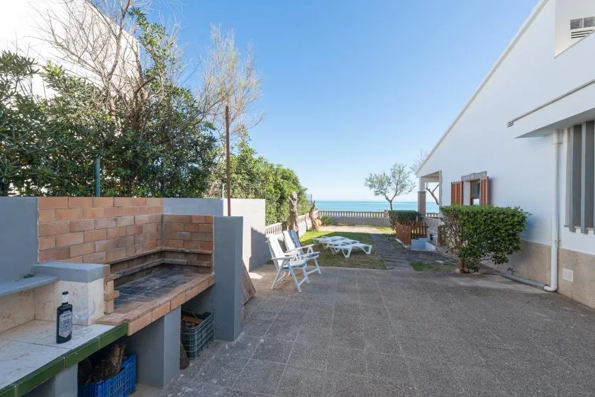 A paved outdoor patio with built-in seating, greenery, and a view of the sea.