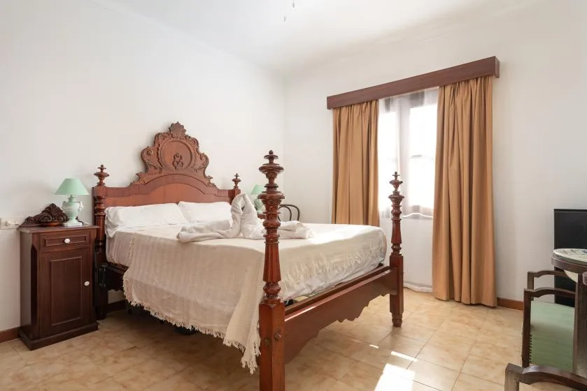 A bedroom with an ornate wooden bed and tan curtains beside a window.