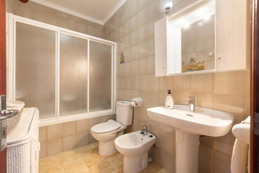 A tiled bathroom with a bathtub, toilet, bidet, and wall-mounted sink.