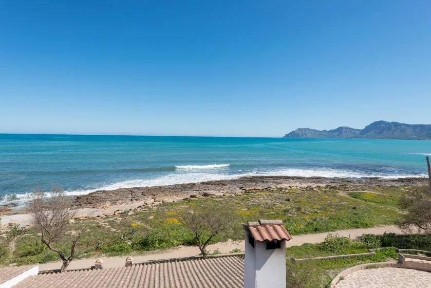 A coastal landscape with turquoise water, a sandy shoreline, and distant hills.