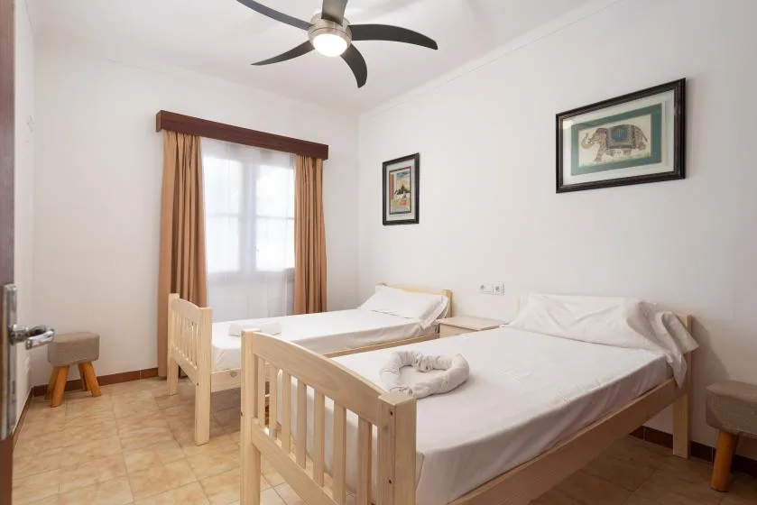 A bright bedroom with two single beds and a window with curtains.