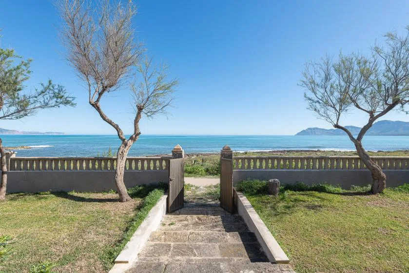 A stone path leads through a garden gate toward the sea.