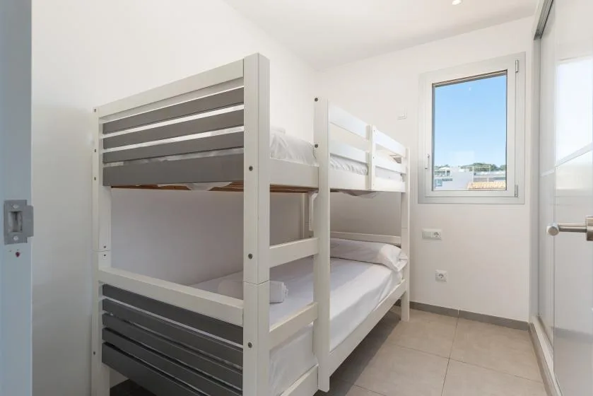 A bright bedroom with a white bunk bed and a window.