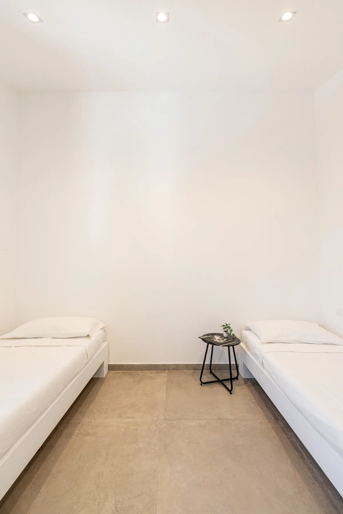 Un dormitorio luminoso con dos camas y una mesita entre ellas.