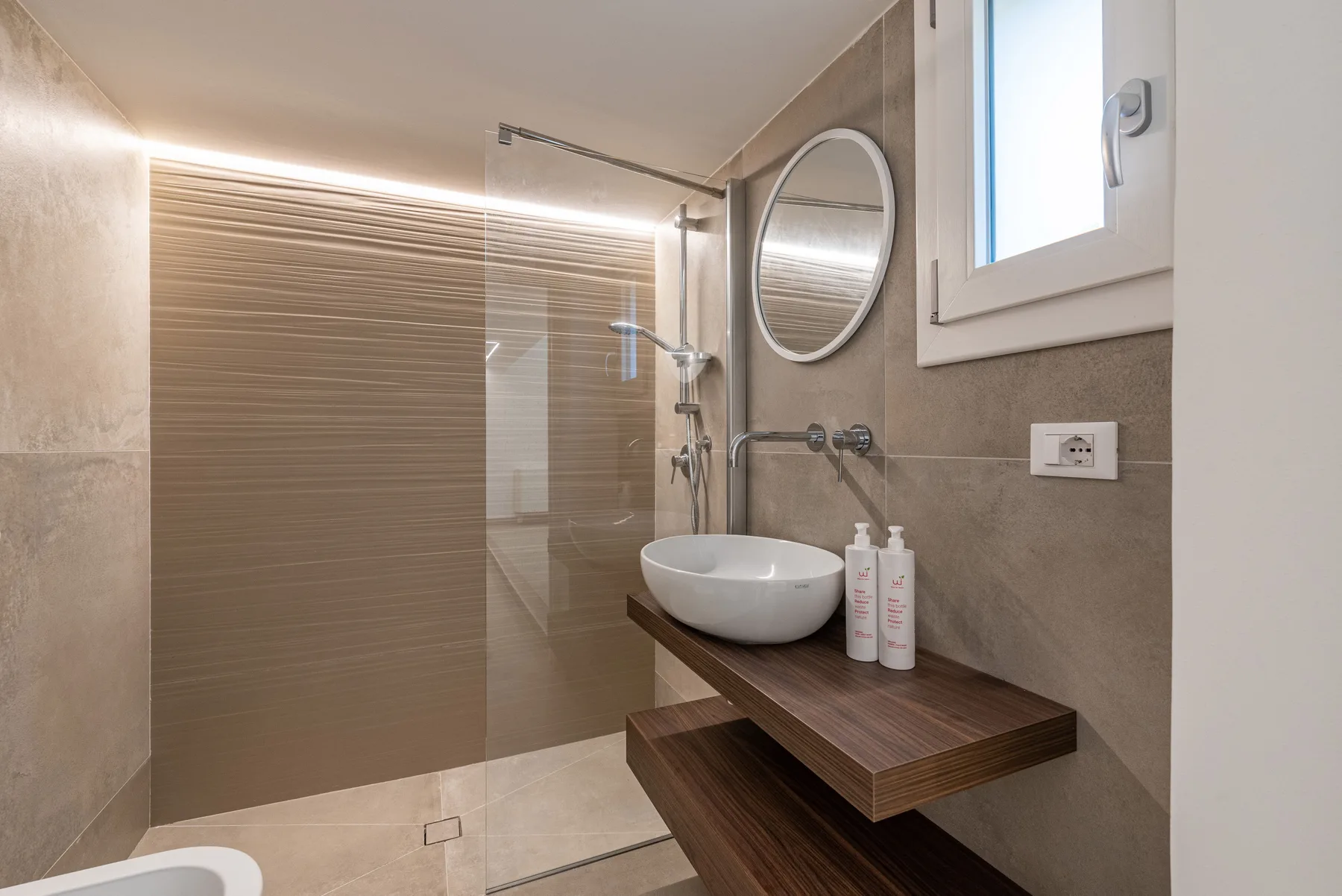 Un baño moderno con ducha de vidrio, lavabo suspendido y espejo redondo.