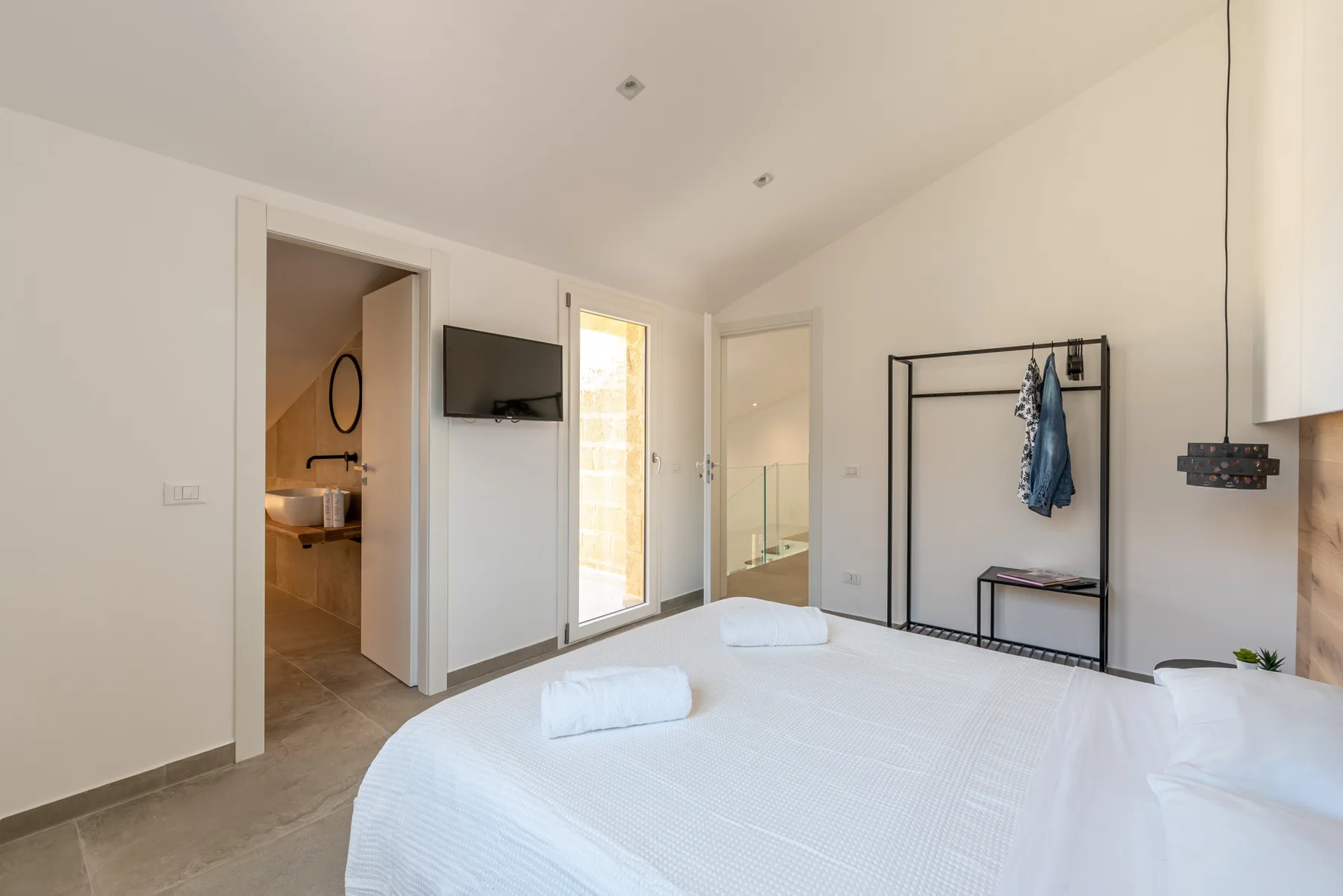 Un dormitorio luminoso con una cama tendida y una puerta abierta hacia el baño.