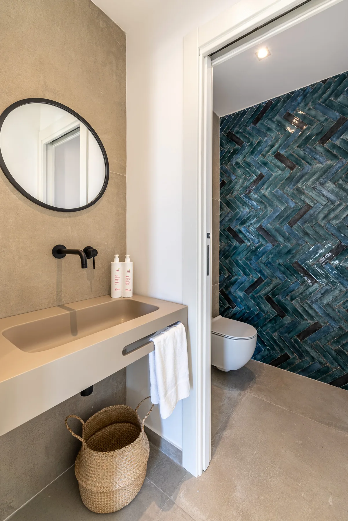 Un lavabo de baño con espejo redondo está junto a una zona de ducha con paredes azules estampadas.