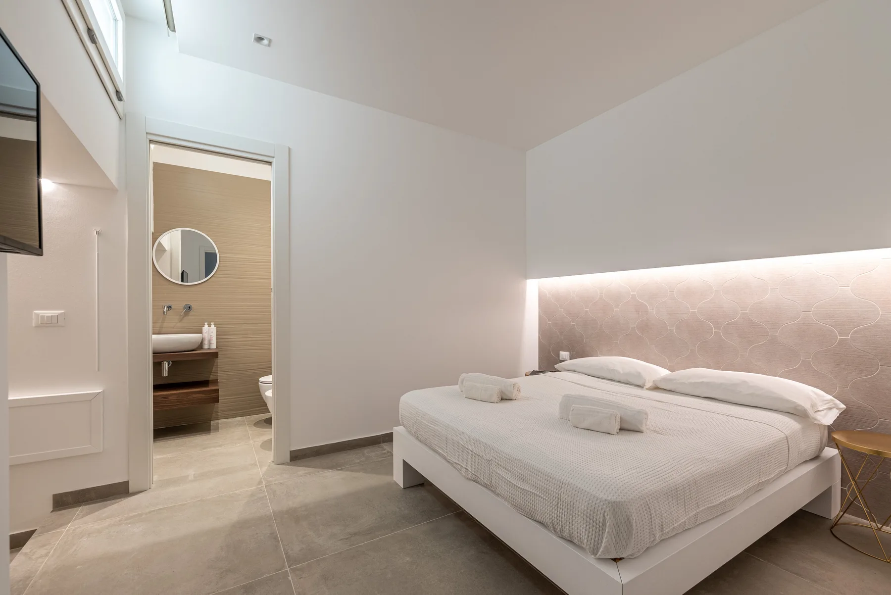 Un dormitorio con una cama bien arreglada y una puerta abierta hacia el baño.