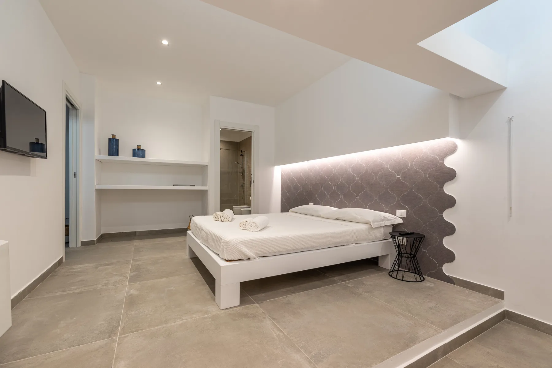 Un dormitorio moderno con una cama blanca y un panel de pared suavemente iluminado.