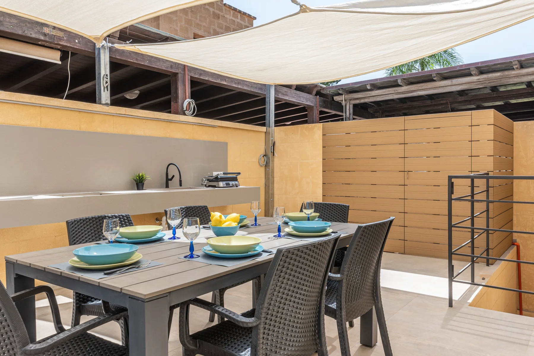 Comedor al aire libre con una mesa preparada bajo una cubierta de sombra.