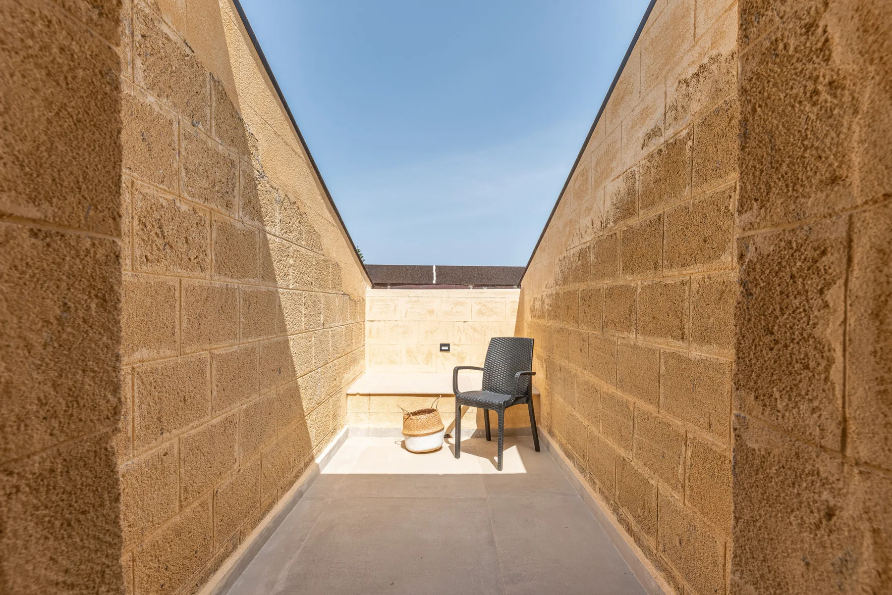 Una terraza exterior estrecha con una silla y una maceta entre paredes de piedra.