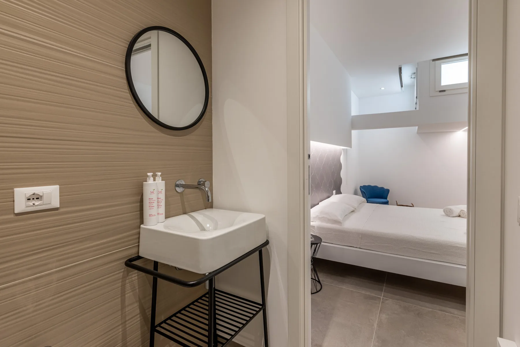 Un área de lavabo da paso a un dormitorio con una cama.