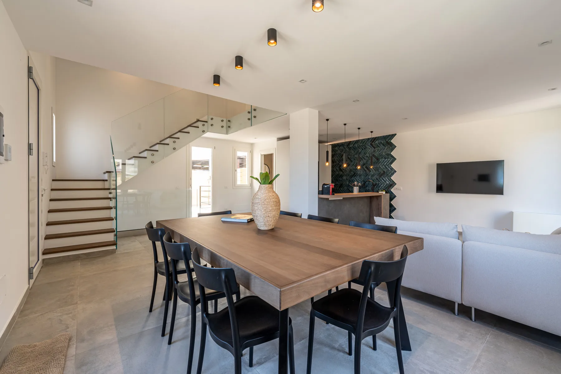 Comedor con una mesa larga de madera y sillas negras junto a una sala de estar.
