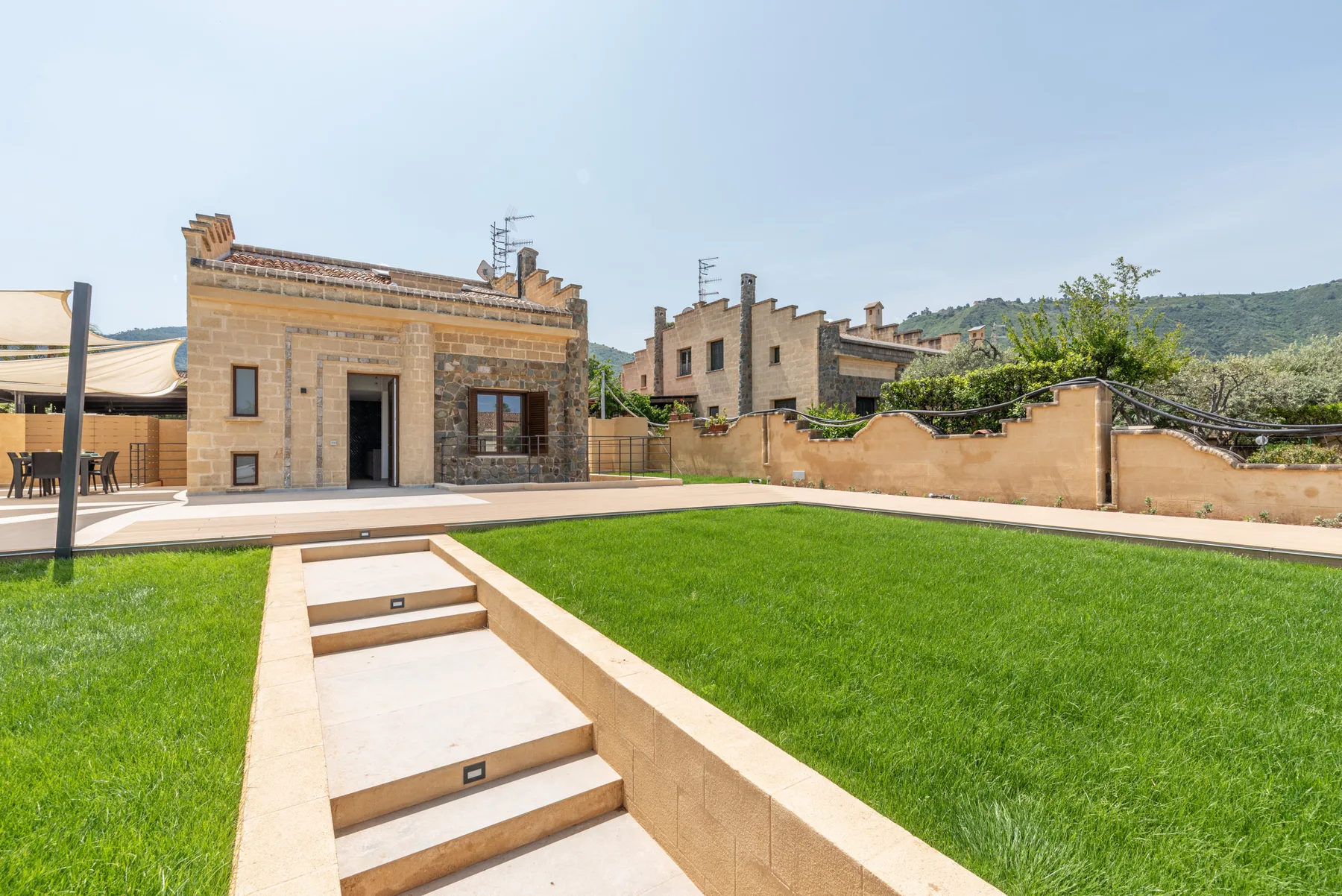 Zona exterior ajardinada con césped verde, escalones y edificios de piedra.