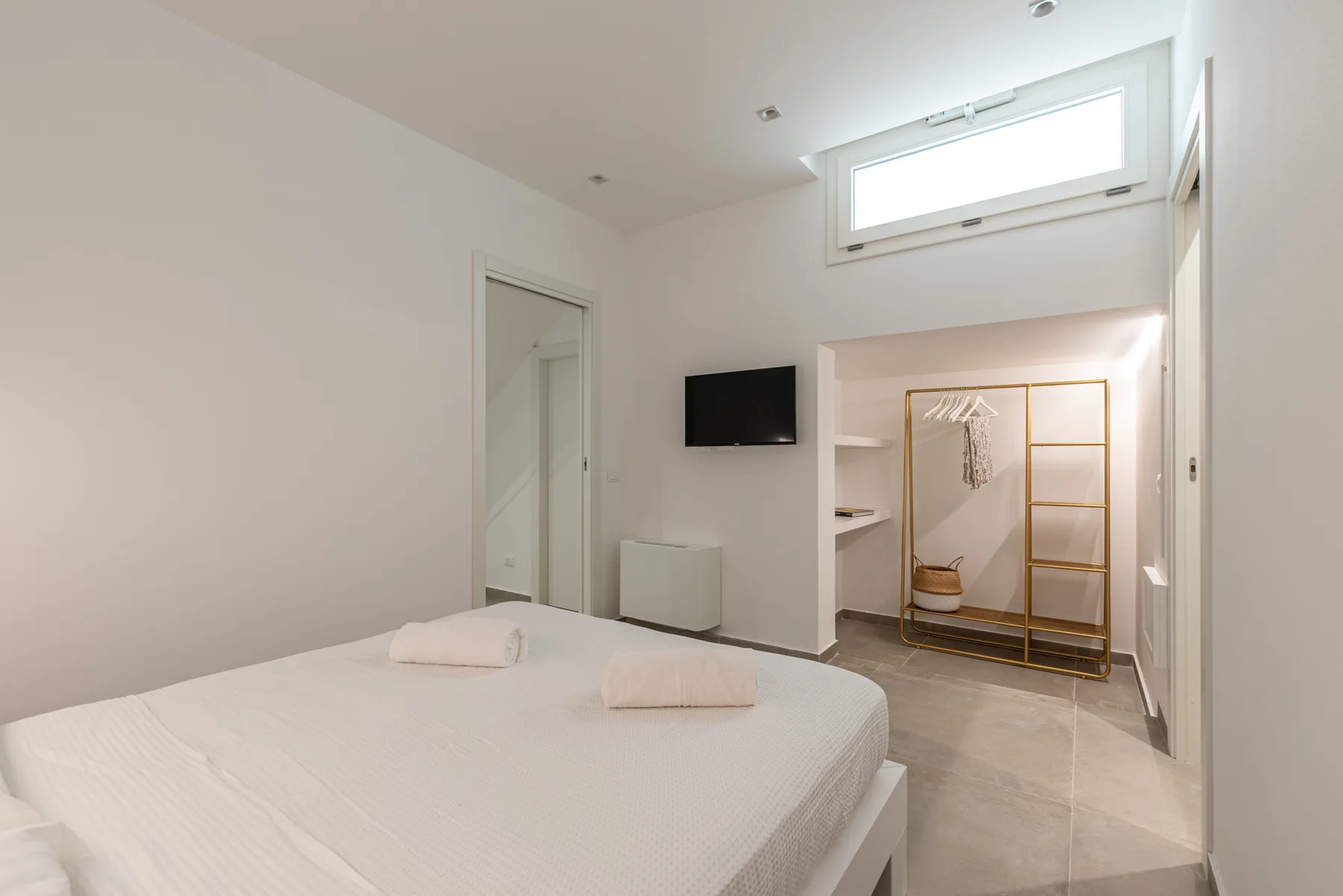 Un dormitorio luminoso con una cama, un televisor en la pared y un armario abierto.