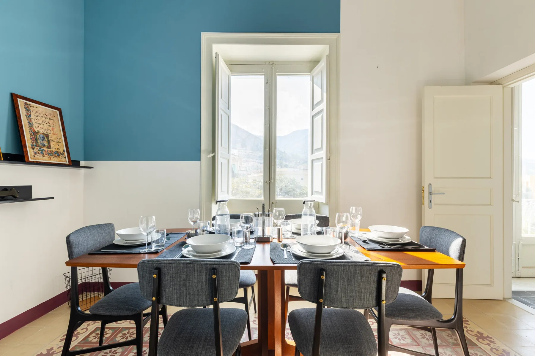 Comedor con una mesa puesta con vajilla junto a una ventana amplia.