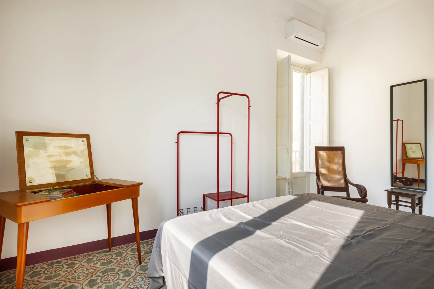 Un dormitorio luminoso con una cama, una estructura metálica roja y un escritorio de madera.
