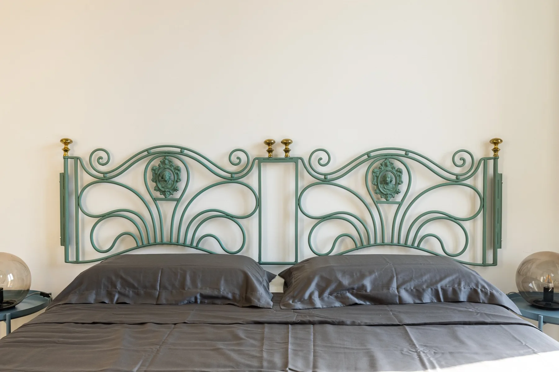 Un dormitorio con una cama bajo un cabecero de metal verde ornamentado.