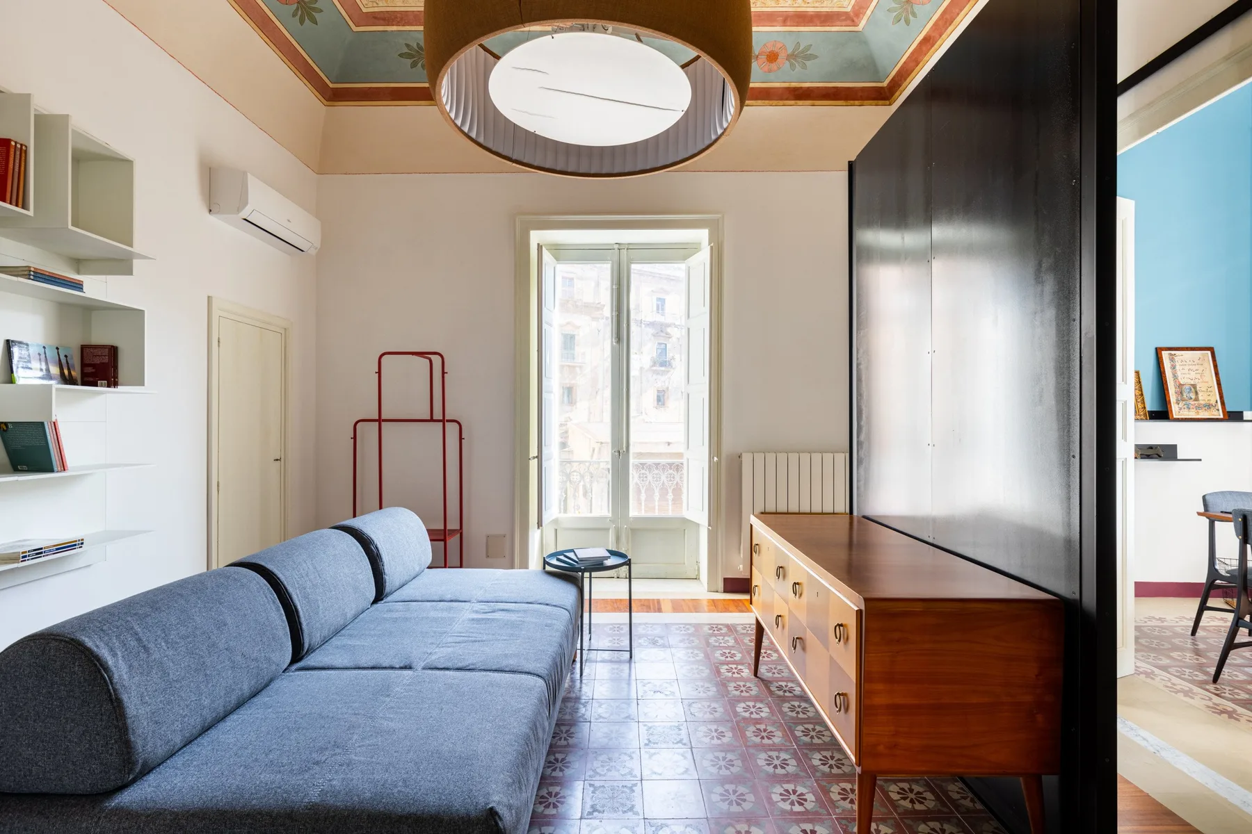 Una sala de estar con asientos azules, suelo de baldosas estampadas y una ventana.