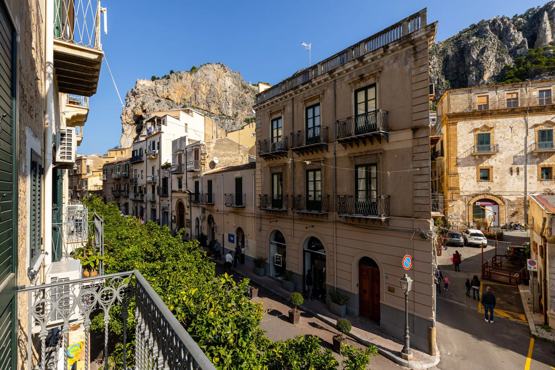 Vista de una calle con edificios próximos y una colina rocosa al fondo.
