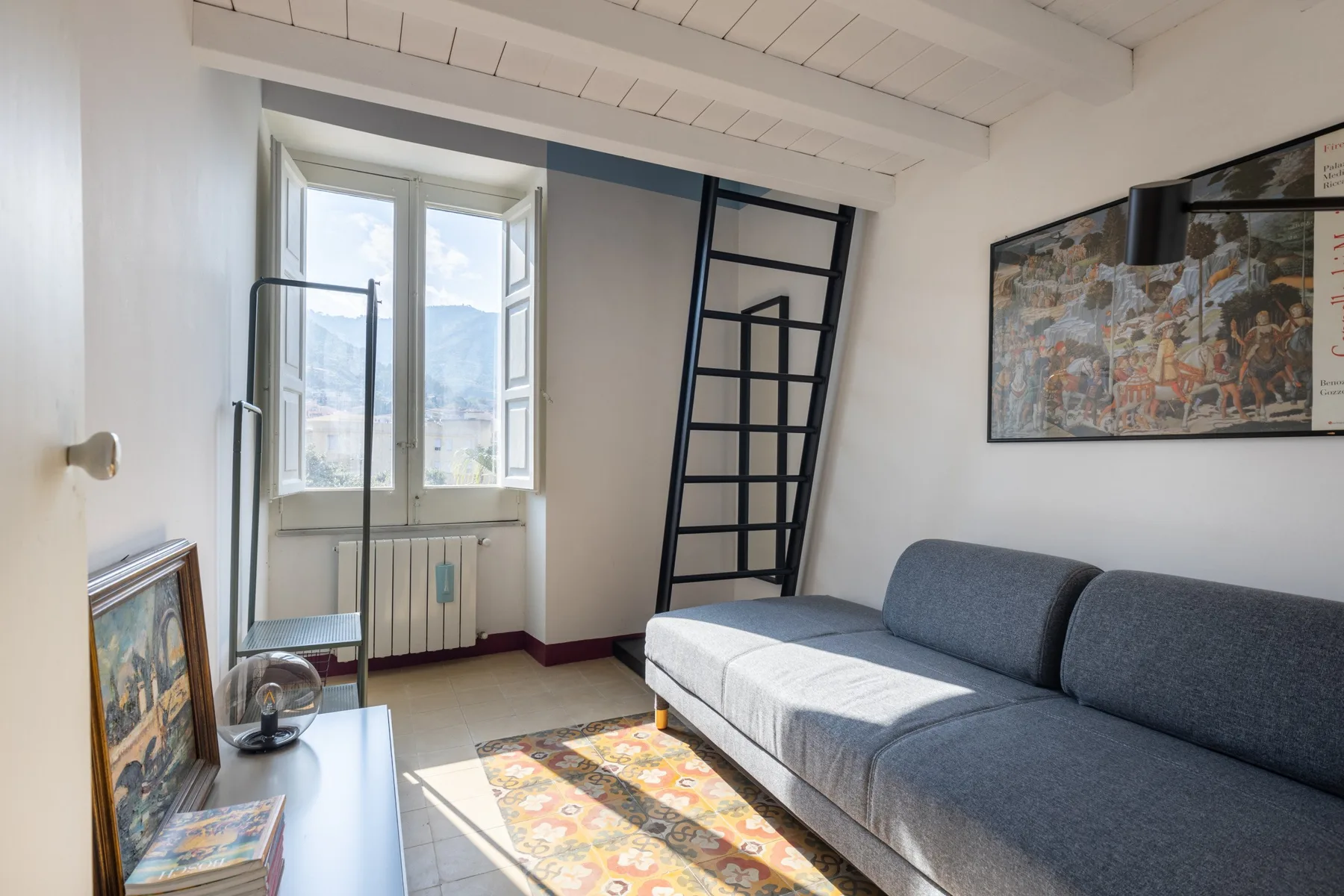 Una sala luminosa con un sofá gris junto a una ventana abierta.