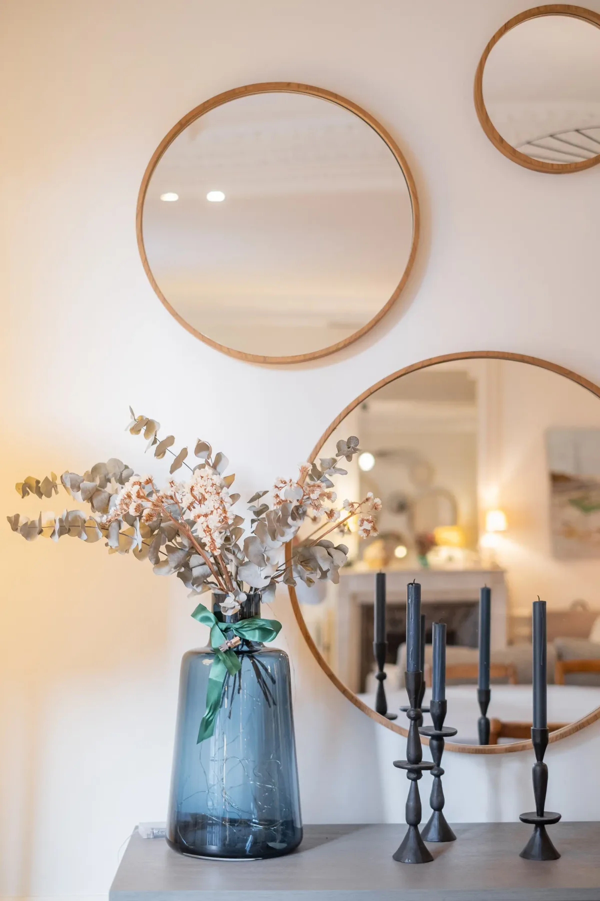 A decorative arrangement and candle holders sit on a console beneath round mirrors.