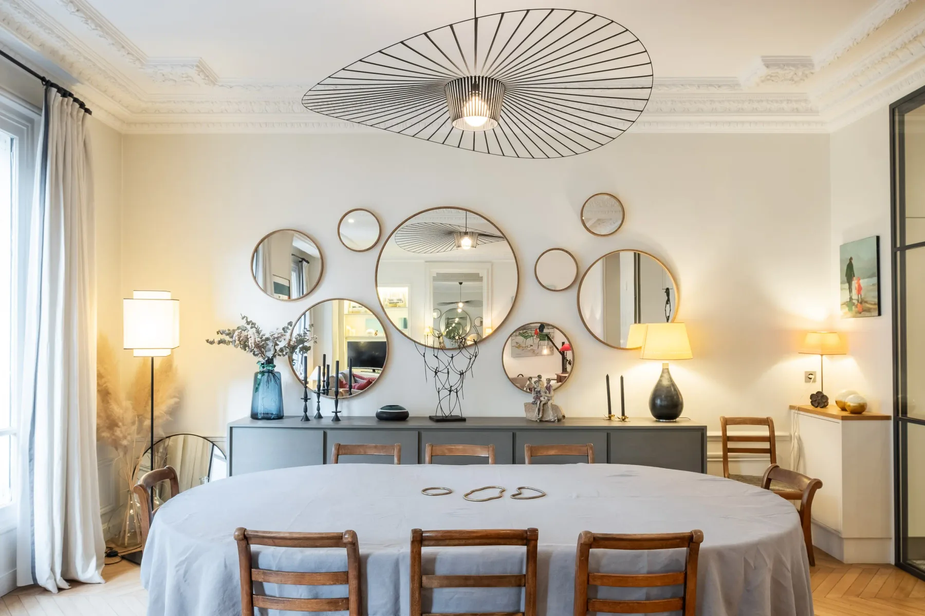 A bright dining room with a round table and mirrors above a sideboard.