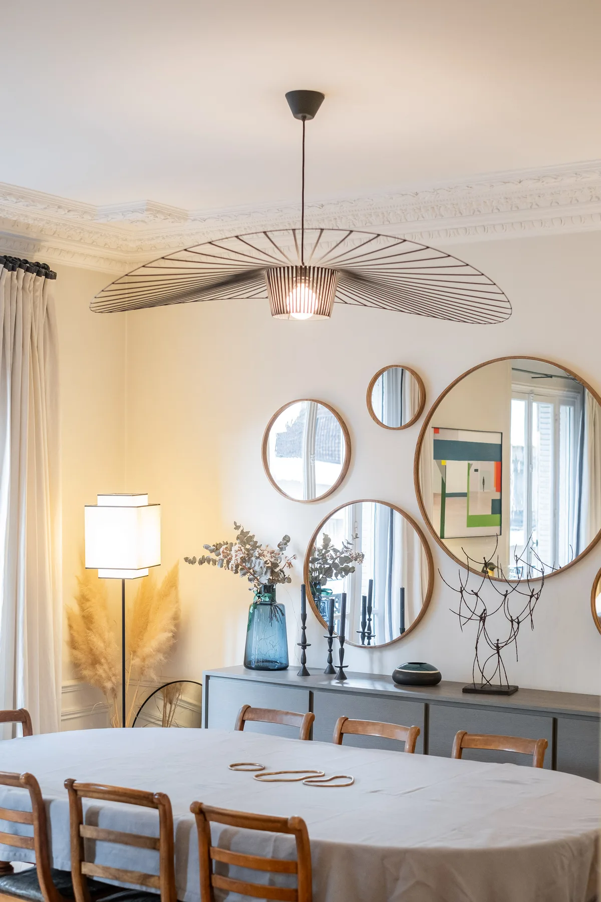 A dining room with a table, wall mirrors, and a wide pendant light.