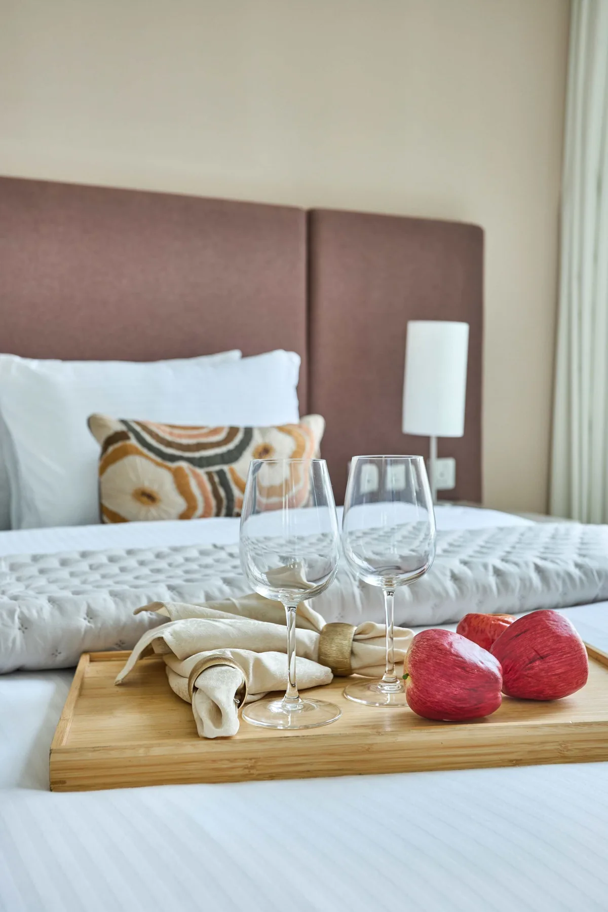 Un dormitorio con una cama bien tendida y una bandeja con copas y fruta.