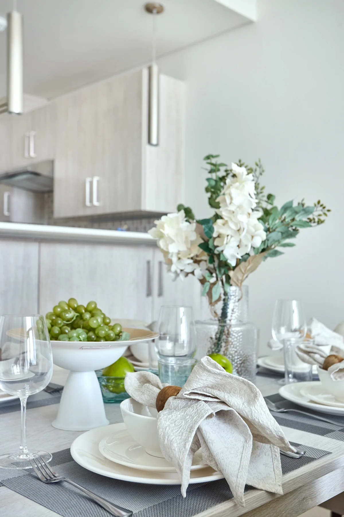 Una mesa está puesta con platos, servilletas dobladas, copas, fruta y flores.