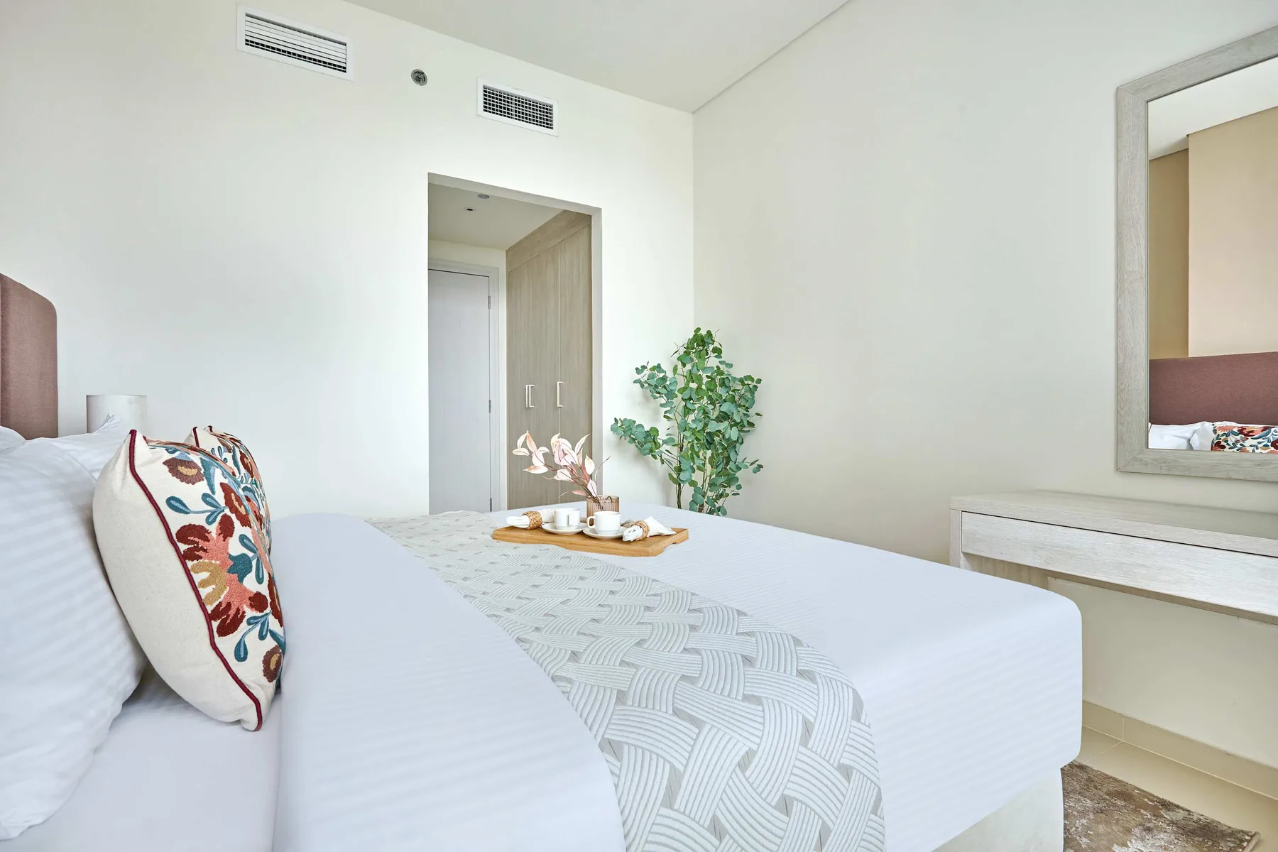 Un dormitorio luminoso con ropa de cama blanca y un cojín decorativo.